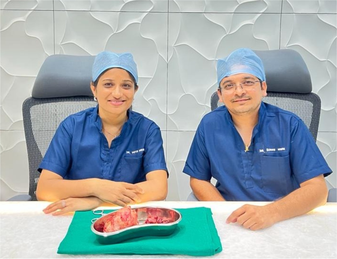 Dr. Sunny Nayak in surgical scrubs, seated beside a surgical specimen on a tray, smiling post-operation.