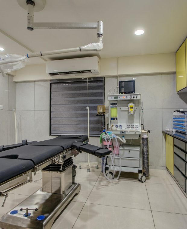 Modern operation room with advanced surgical table, anesthesia machine, overhead lighting, and organized medical storage cabinets.