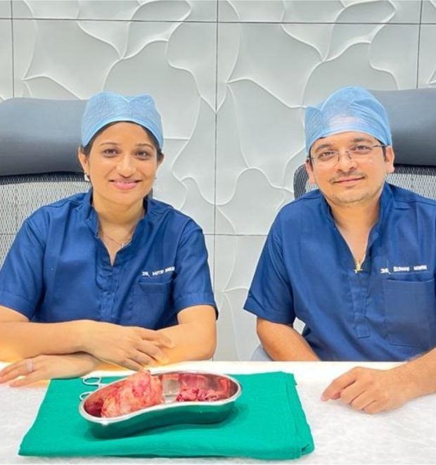 Expert Surgical Team – Dr. Mitsu Harani Trivedi & Dr. Sunny Nayak Dr. Mitsu Harani Trivedi and Dr. Sunny Nayak in surgical scrubs, seated beside a surgical specimen on a tray, smiling post-operation.